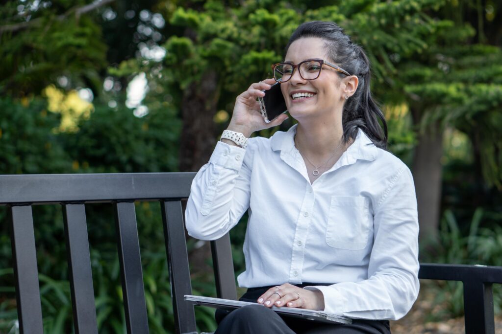 corporate headshot of a woman speaking on the phone and smiling while sitting at the park