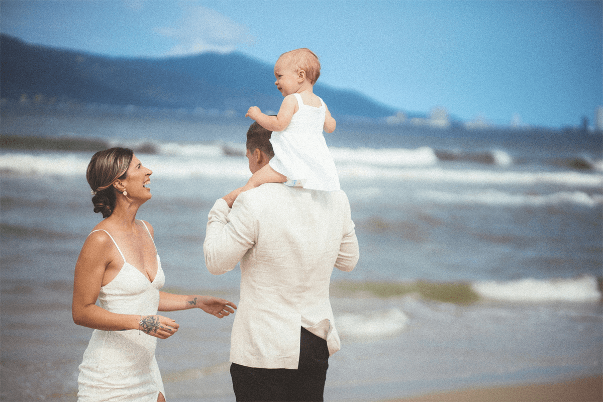 candid moment of beach wedding couple playing with baby daughter during family photo session in Brisbane