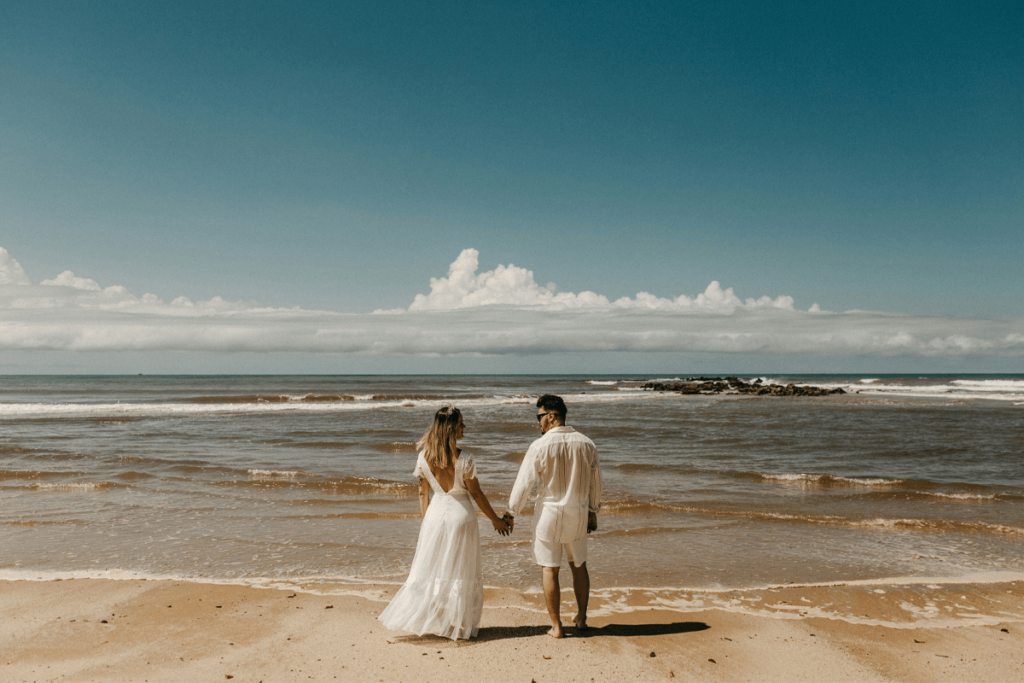 wedding couple holding hands and walking toward the ocean at quiet beach in Brisbane