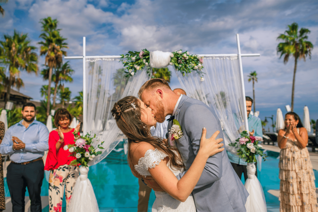 bride and groom sharing their first kiss at an outdoor poolside ceremony in Brisbane with guests applauding